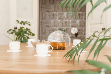 A cozy composition featuring a teapot and cups on a round wooden table, complemented by green plants and soft lighting in a tastefully designed interior space.