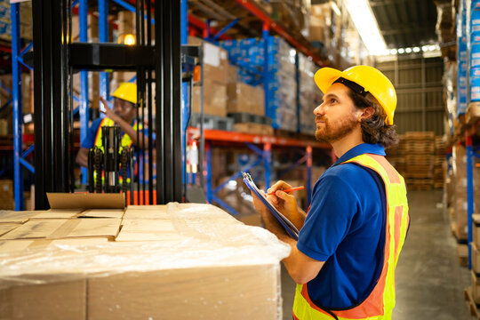 A warehouse worker inspects inventory with a clipboard, ensuring efficient operations and safety in a busy environment. - Powered by Adobe
