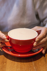 A cozy scene showing hands holding a red cup of a beverage on a wooden surface, highlighting a warm and inviting ambiance.