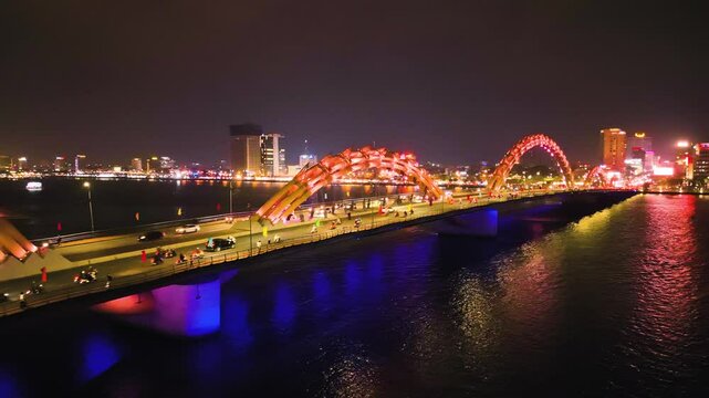 Glowing orange dragon bridge arching over han river, illuminating da nang nightscape with dramatic architectural silhouette and reflective water surface