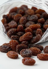 Fototapeta premium Pouring Raisins From Plastic Bag on White Surface for Snacking