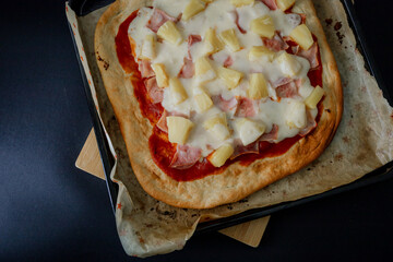 Square Hawaiian pizza with ham and pineapple, presented on a black background in a dark food style....