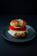  A juicy beef burger with cucumber, tomato, and lettuce, styled in dark food aesthetics on a black plate. Captured in a vertical format for a striking visual.