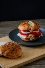  A juicy beef burger with cucumber, tomato, and lettuce, styled in dark food aesthetics on a black plate. Captured in a vertical format for a striking visual.
