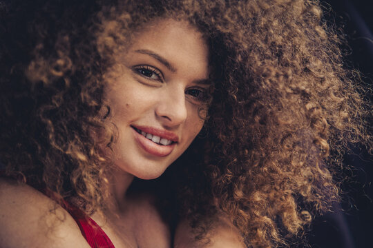 Portrait of a smiling young woman with curly hair showcasing natural beauty and confidence in a studio setting