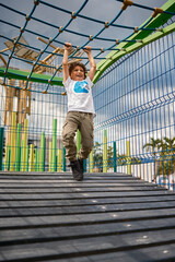 Child having fun climbing on rope bridge at playground