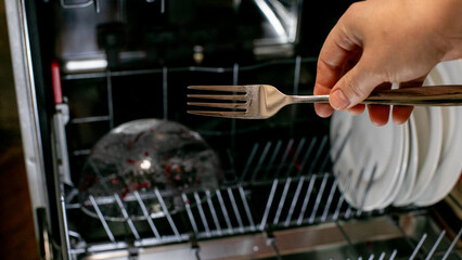 Hand placing fork into open dishwasher, kitchen cleaning concept, daily chores, household efficiency