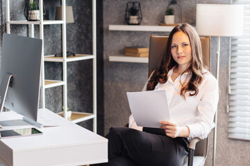 A businesswoman sits at her desk in the office, holding documents and analyzing information.