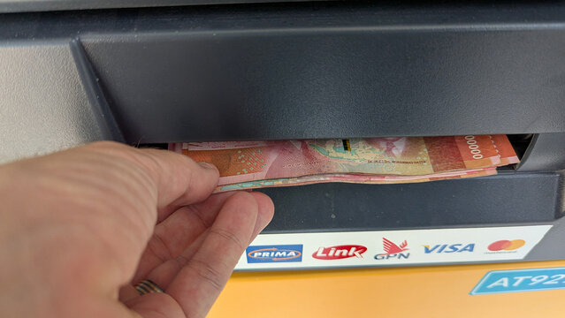 Closeup of hand taking money Indonesian rupiah currency cash from ATM machine in Indonesia - taken on 25th November 2024