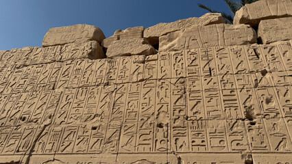Ancient Egyptian Hieroglyphs Carved on Temple Stone Wall under Clear Blue Sky