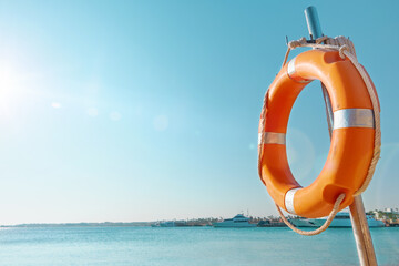 Lifebuoy circle. Scenic view of red and white lifebuoy on post on seaside beach. Scenery landscape of sea ocean shore on sunny day. Water rescue concept.