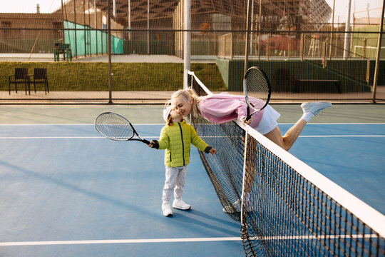 Mother and little son playfully kissing over a tennis net.