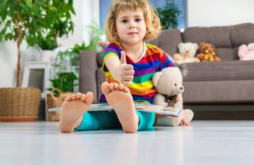 Fototapeta premium Child reading a book at home with a teddy bear at home. Selective focus.