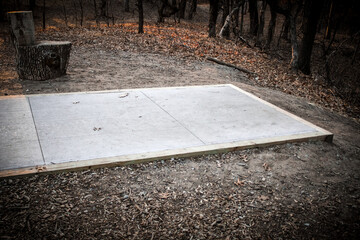 a concrete tee pad, for disc golf, shed or other structure, set in a wooded area. © mailcaroline