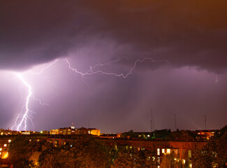 A powerful thunderstorm over the city at night. Bright lightning bolts tear through the dark sky,...