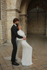 A newlywed couple poses for a wedding photoshoot in a historic Croatian setting. The groom in a...