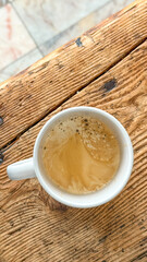 Crema-topped espresso in a white cup on rustic wooden table, cozy morning coffee ritual