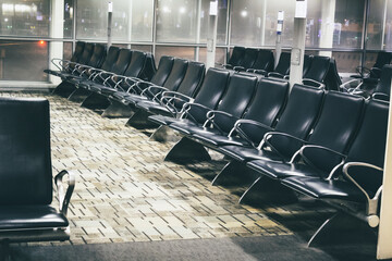 Fototapeta premium a row of vacant seats in an airport gate waiting area at night in diminishing perspective. seating at terminal. windows in view. furniture design element.