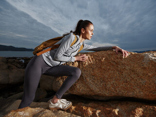 Young female hiker climbing on rocky terrain during overcast day, showcasing determination and...