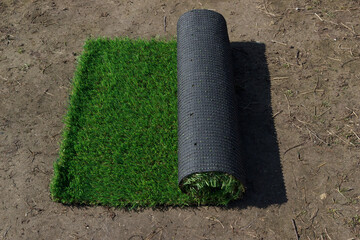 The roll of synthetic grass on the natural ground in garden. The artificial cover backyard.