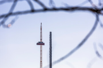 A wind turbine under construction stands next to a fully assembled one, symbolizing progress in renewable energy. The scene captures the transition to sustainable power as the nacelle is being lifted 