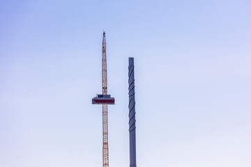 A wind turbine under construction stands next to a fully assembled one, symbolizing progress in renewable energy. The scene captures the transition to sustainable power as the nacelle is being lifted 