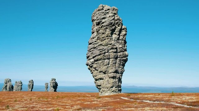 Majestic manpupuner rock formations stand tall against a vibrant blue sky, showcasing komi republic's unique natural beauty with red-toned vegetation covering the ground