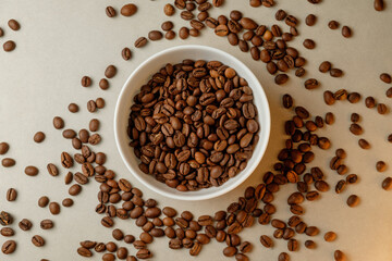 Perfectly roasted coffee beans scattered around a bowl on a light background