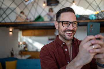 Happy father using smartphone at home while children playing upstairs