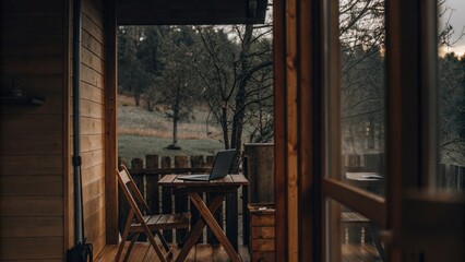 an inviting cabin's open doorway revealing a laptop set on a table overlooking a serene landscape