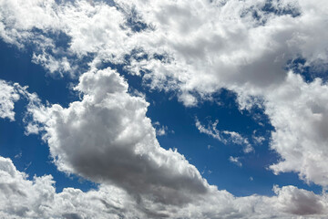 Obraz premium Bright blue sky with fluffy white clouds. Beautiful cloudscape peaceful atmosphere. Natural summer sky with soft sunlight and clear weather. From beneath view. Looking up the sky.