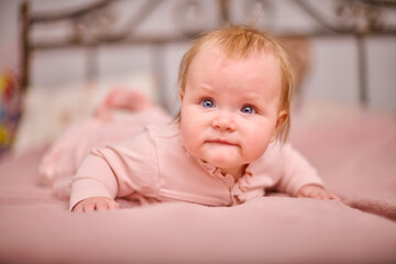 Baby girl, blonde, blue eyes, lies on soft pink bedspread, curious expression, warm lighting, cozy...