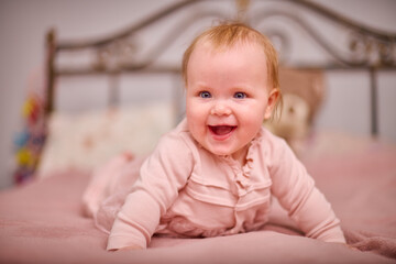 Naklejka premium Young female with blonde hair, light skin, smiles joyfully while lying on pink bed. Soft lighting and ornate headboard create cozy, warm atmosphere