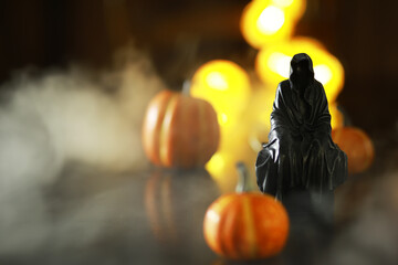 Eerie Halloween Display with Mysterious Cloaked Figurine and Pumpkins in Smoky Atmosphere