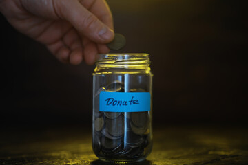 Hand Donating Coins into Jar for Charity with Blue Label