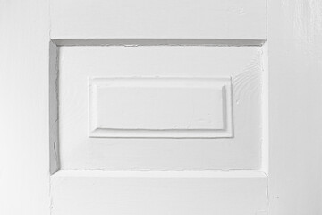 Old wooden door painted white closeup. Rectangular carved design with aged texture. Vintage carpentry background. Classic craftsmanship and rustic character. Empty copy space white wood.