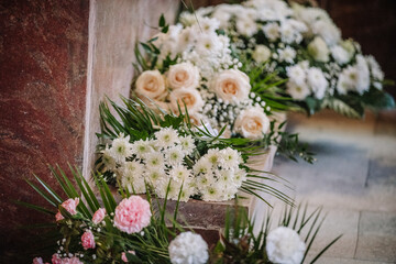Close-up of elegant white and cream funeral flower arrangements placed beside a coffin inside a church, symbolizing remembrance and sympathy..