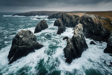 Obraz premium Rocky coastline of the Isle of Wight, featuring rugged cliffs and crashing waves against the shore. Piercing aerial view of jagged rocks amidst raging sea waves .