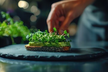 Chef's hand garnishing avocado toast with fresh microgreens on a slate plate, showcasing a healthy and delicious meal.