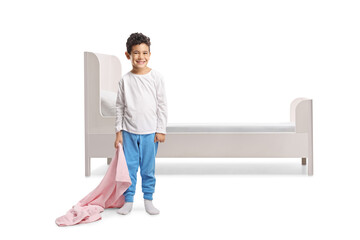 Boy in pajamas holding a soft security blanket in front of a bed