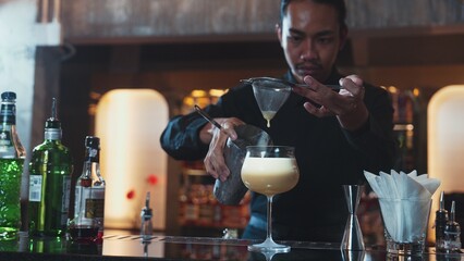 Asian bartender using strainer all ingredients alcohol liquor and syrup tasty in cocktail glass with ice serving special refresh drink showcasing nightlife mixology at luxurious nightclub. Vinosity.