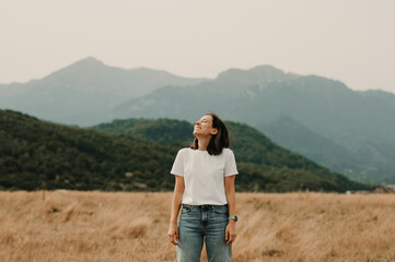 A woman stands peacefully in a vast field, gazing at the majestic mountains in the serene embrace...