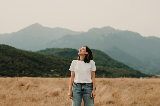 A woman stands peacefully in a vast field, gazing at the majestic mountains in the serene embrace of nature