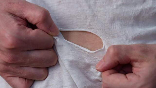A man inspecting a ripped t-shirt that he is wearing. Close up.