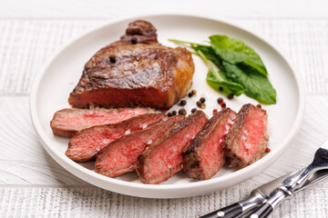 A perfectly cooked sliced striploin steak with a juicy, tender texture, served alongside a glass of rich red wine