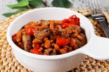 Baked beans with sausage and red pepper in a traditional white baked bean dish with a handle