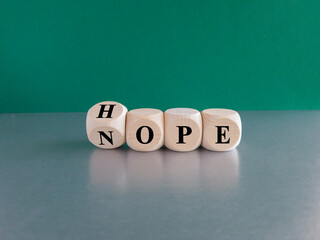 Hope or nope symbol. Turned a wooden cube and changes the word 'nope' to 'hope'. Beautiful green background, gray table. Business and hope or nope concept.