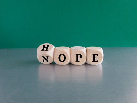 Hope or nope symbol. Turned a wooden cube and changes the word 'nope' to 'hope'. Beautiful green background, gray table. Business and hope or nope concept.