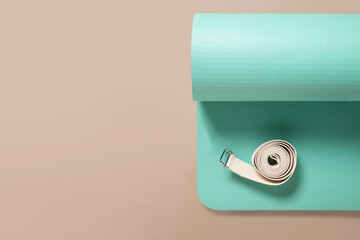 Green yoga mat and white strap on beige background. Relaxation and meditation concept. Accessories for yoga practice. Top view. Copy space.