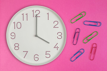 Clock showing four o’clock with colorful paper clips on pink background. Productivity concept with 16 o'clock clock and tools for office work, school tasks, and deadline management.